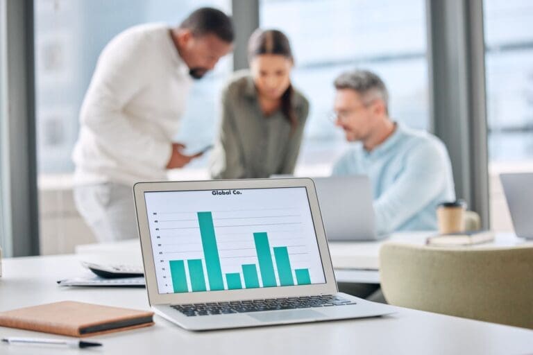 Shot of a laptop with graphs on display in an office with businesspeople working in the background.